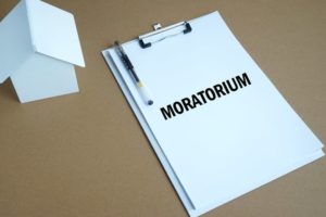 A white paper house sits next to a sheet of paper on a clipboard reads Moratorium