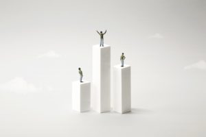 Three cartoon figures stand on plinths of different heights, representing a property manager elevating themselves above table stakes positioning.