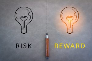 A dark lightbulb is on the left above the word risk. On the right is a lit bulb above the word reward.