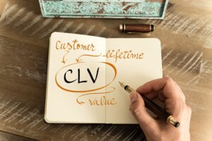 CLV is written in a notebook and circled in orange. There are also arrows pointing to the letters with the words Customer Lifetime Value.