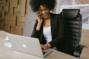 Woman talking on the phone at her desk and smiling happily. This is an example of strong communication that is important in the acquisition of a business.